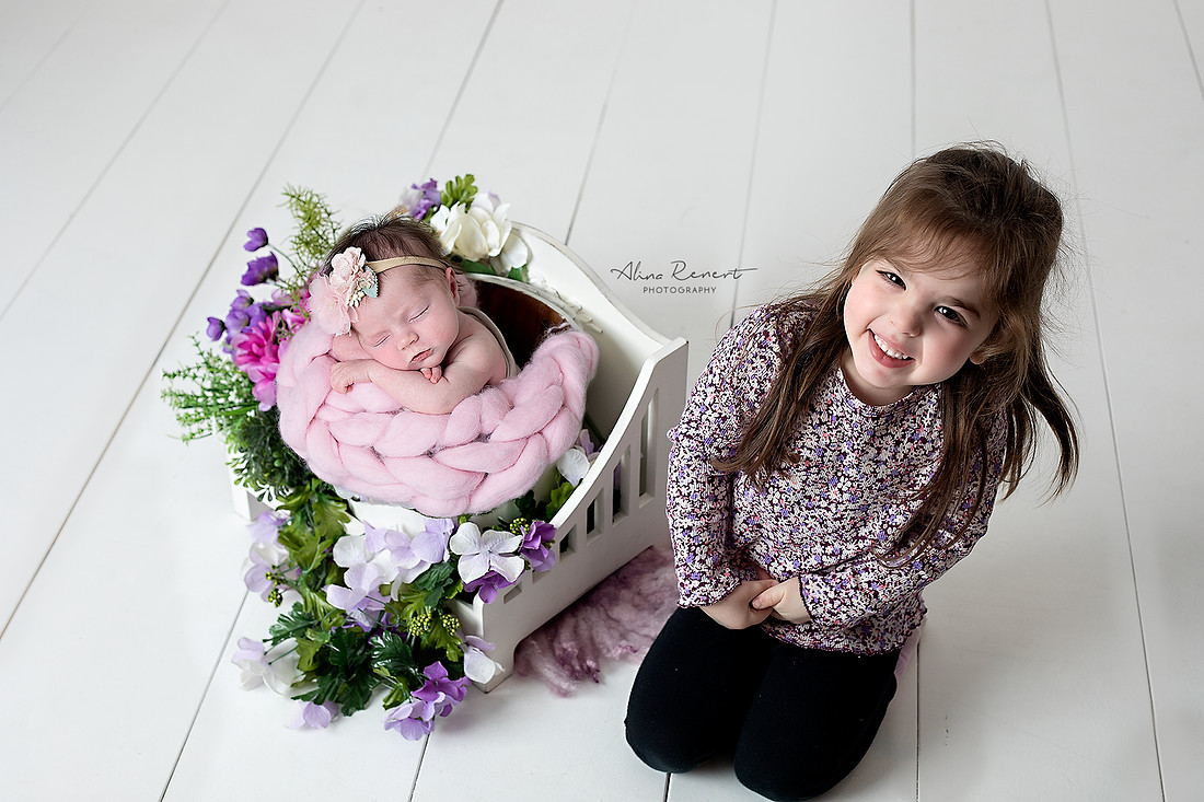 Sibling newborn photography, Wheeling, IL, featuring big sister Alina and newborn baby Daniella with a floral prop on white wash wood. Light and airy editing