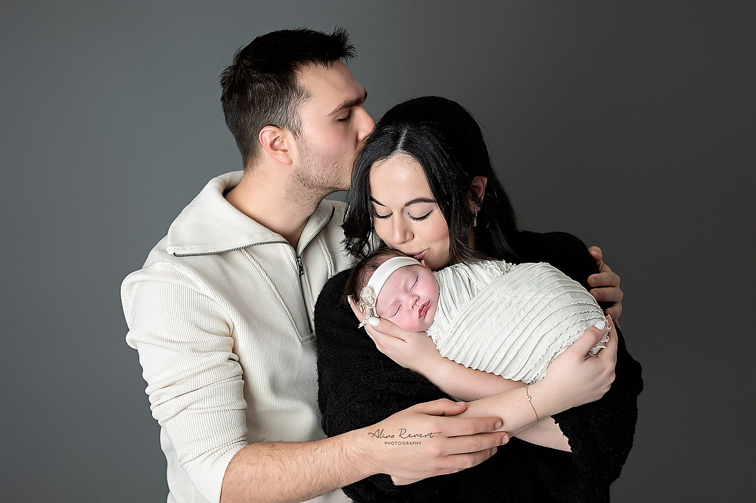 Mom & Dad holding newborn baby girl in a cream textured wrap, studio newborn session, Wheeling, Illinois.